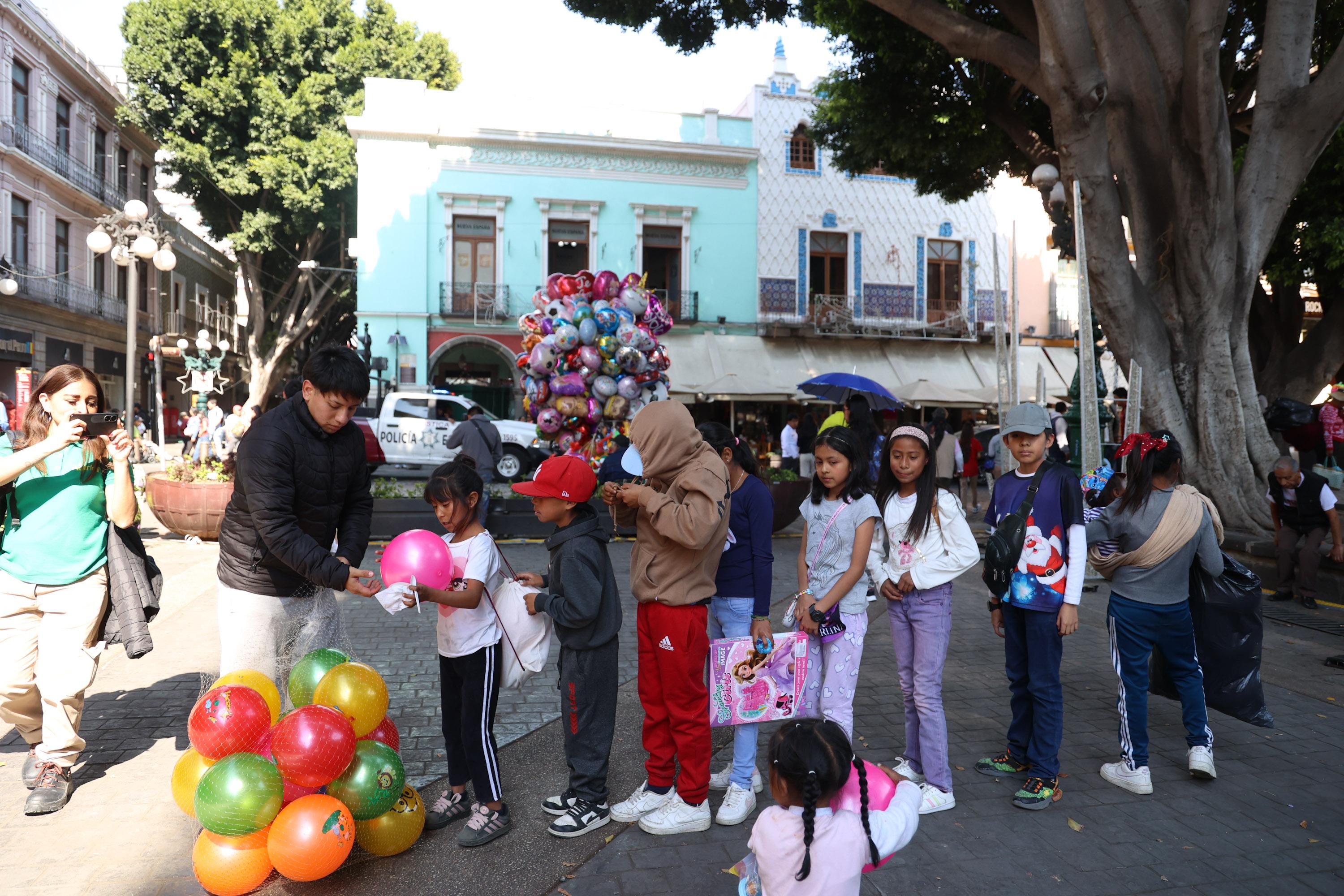 Ayudantes de los Reyes Magos regalan juguetes en el zócalo de Puebla.