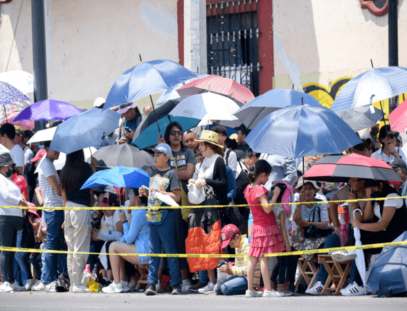 Padres y madres de familia apoyan a las y los estudiantes en el desfile.